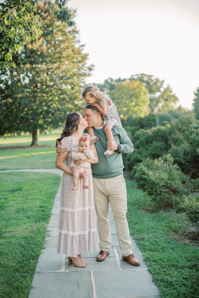 Mother and father kiss as they hold their two daughters at Glenview Mansion MD.