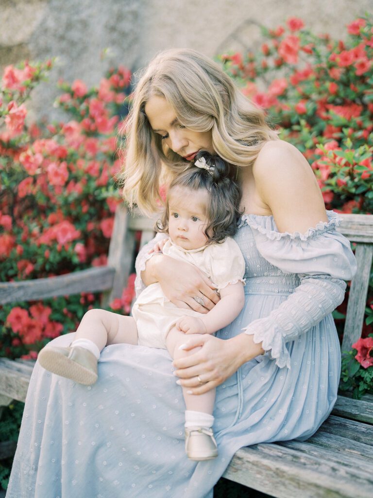 Blonde Mother In Blue Doen Dress Sits On A Bench With Her Baby Daughter At Bishop's Garden.