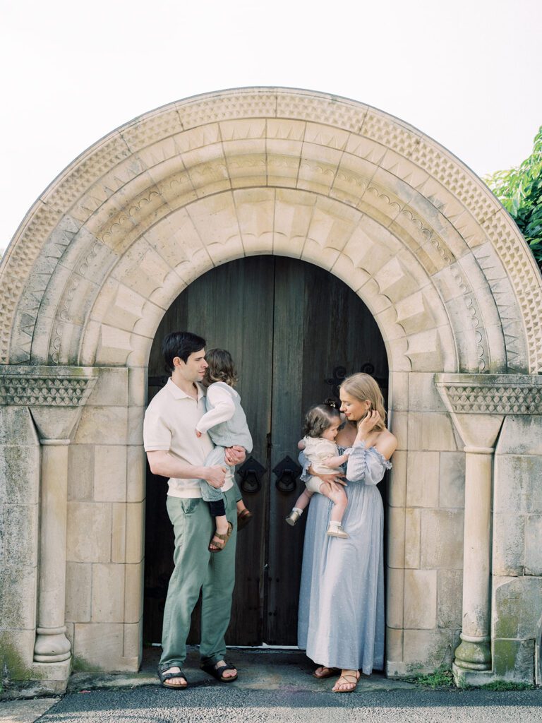 Family Of Four Stand In Front Of The Stone Archway At Bishop's Garden In Washington, D.c.