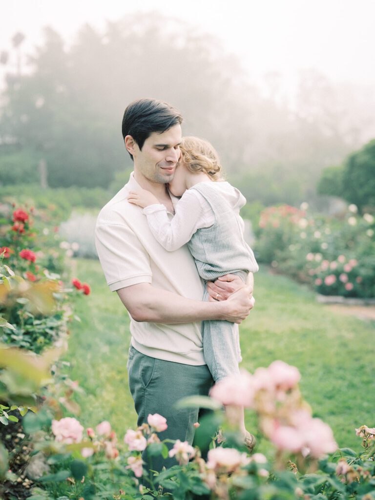 Father Holds His Toddler Son In A Rose Garden.