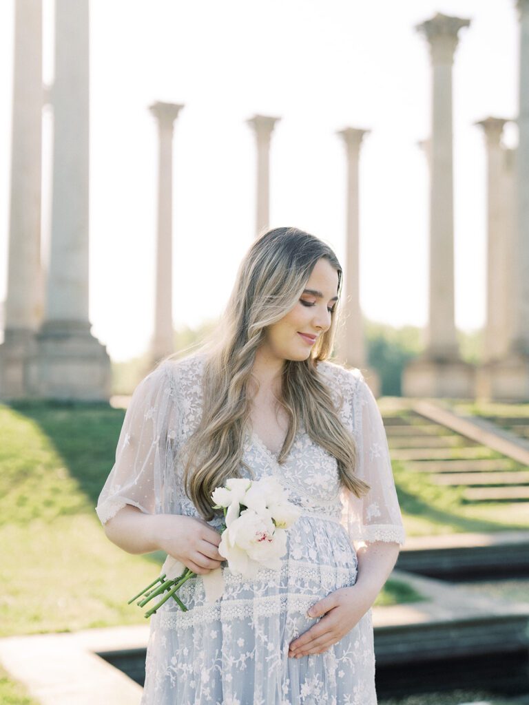 Pregnant Mother Stands Looking Down While Holding A Bouquet Of Flowers During Her Maternity Session At The National Arboretum.