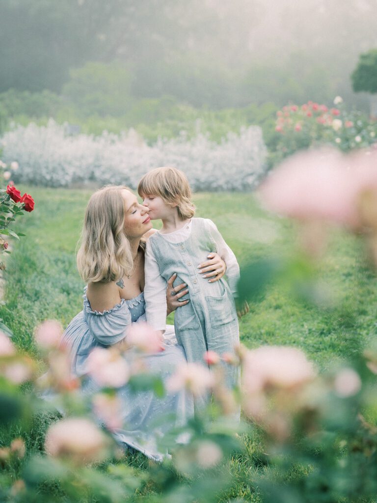 Little Boy Leans Over To Kiss His Mother In Bishop's Garden.