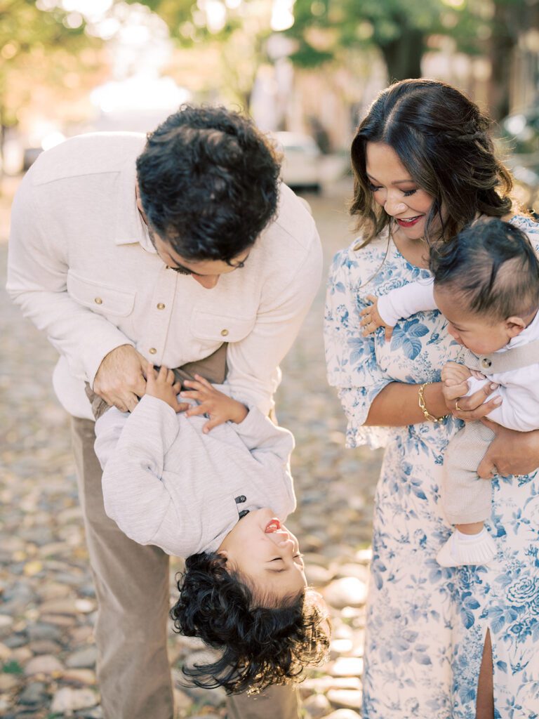 A father holds his son upside down while standing with his wide and other son in Alexandria, VA.