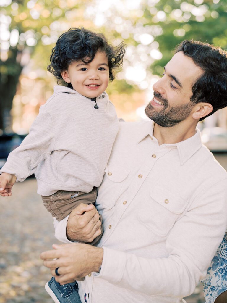 A father holds his young son and smiles.