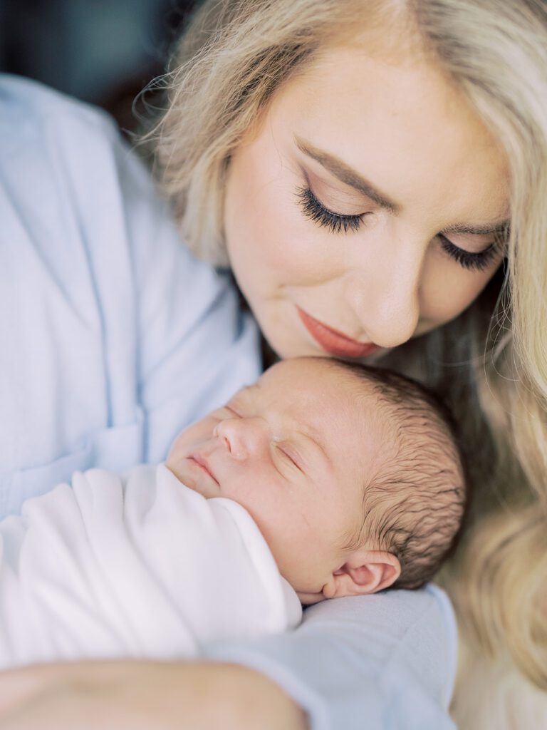 Blonde Mother Leans In To Kiss Her Newborn Baby's Head.