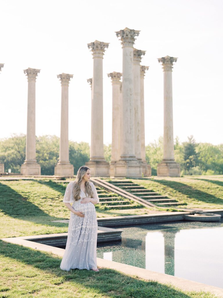 Pregnant Mother Stands Near Pond At The National Arboretum With One Hand On Top Of Her Belly And One Hand Below Her Belly.