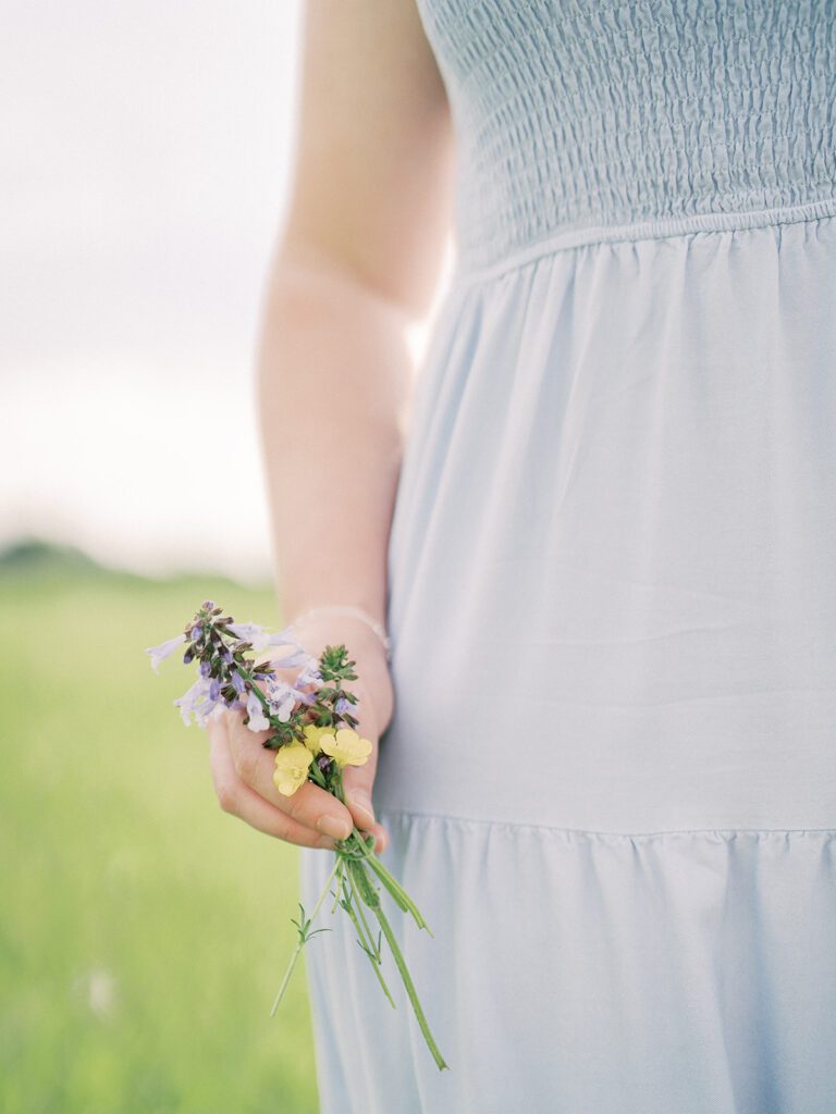 Close-Up View Of Woman In A Blue Dress Holding Purple And Yellow Flowers.