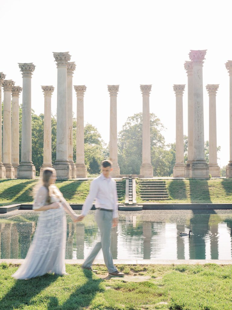 A Blurry Image Of A Pregnant Couple Walking In Front Of The Capital Columns Pond At The National Arboretum.