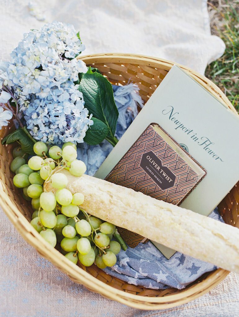 A Basket With Blue Hydrangeas, Green Grapes, A Baguette, And Two Books.