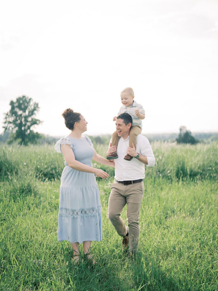 Family Of Three Walk In A Field, Photographed By Manassas Photographer Marie Elizabeth Photography.