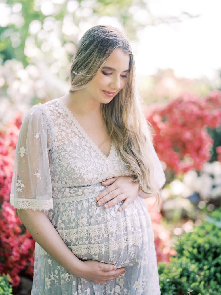 Pregnant Mother Stands With Her Hair To One Side In A Purple Needle &Amp; Thread Gown In An Azalea Garden.