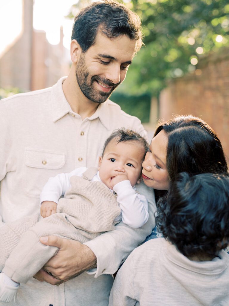 A mother leans in to kiss her baby held by her husband, photographed by Alexandria Photographer, Marie Elizabeth Photography.