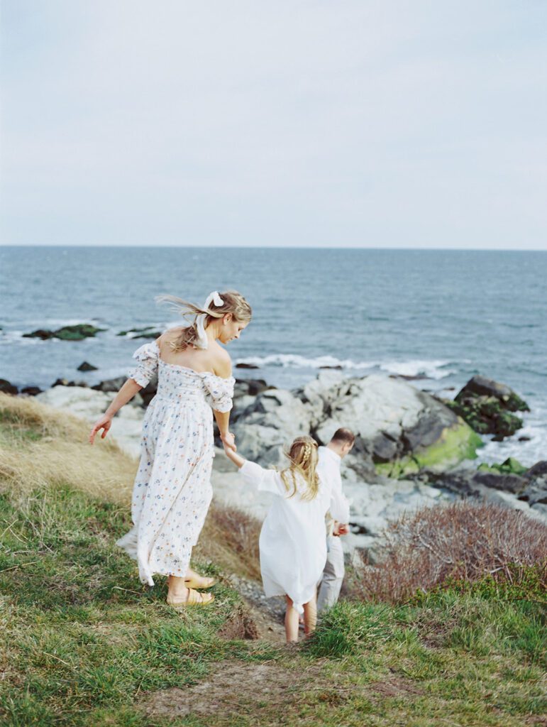 A Mother In A Dress Walking With Her Daughter And Husband Along The Rhode Island Coast, Photographed By Destination Family Photographer, Marie Elizabeth Photography.