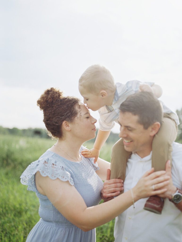 A Little Boy On His Father's Shoulders Leans Down To Kiss His Mother's Head, Photographed By Manassas Photographer Marie Elizabeth Photography.