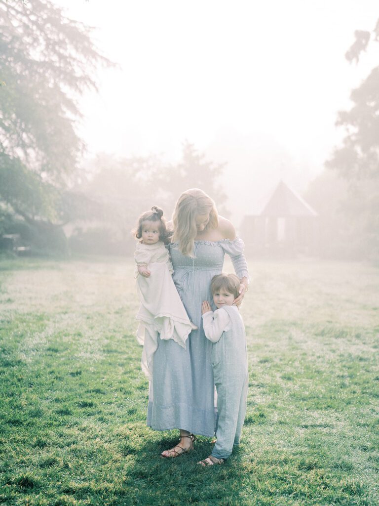 A Mother Stands With Her Son And Daughter In A Foggy Field.