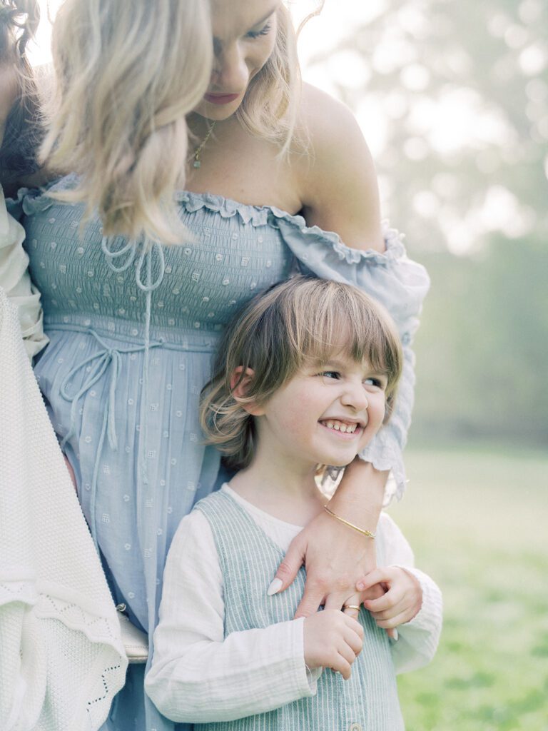 Blonde Mother Places Her Arm Around Her Young Son As He Smiles.