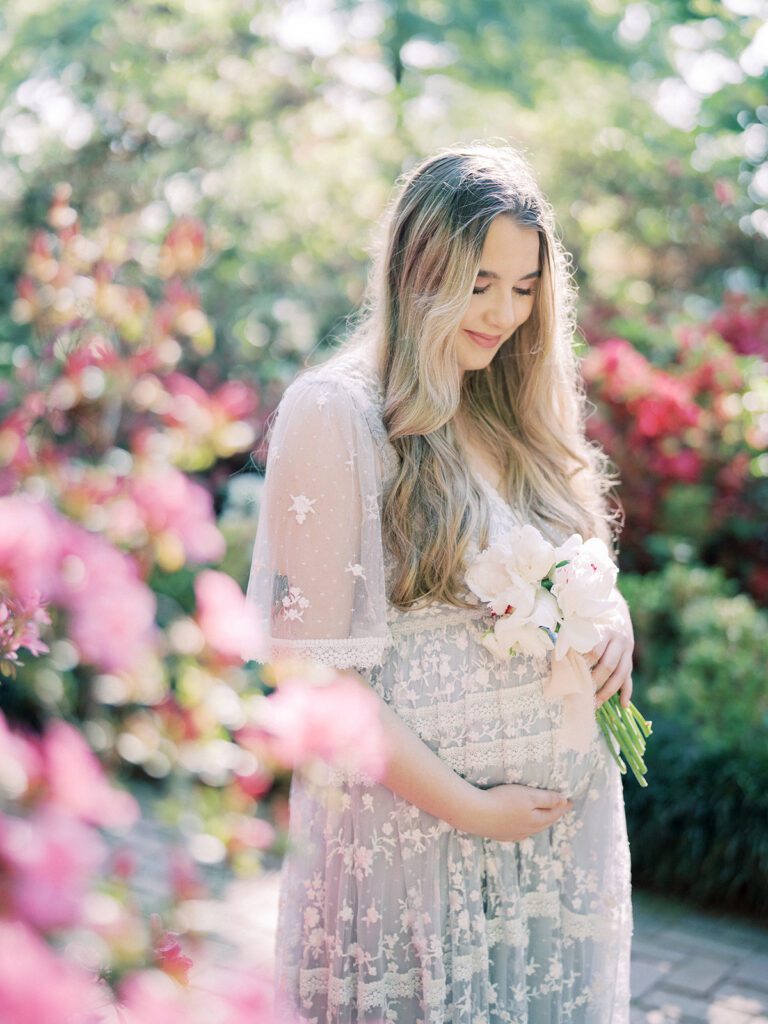 A Pregnant Mother In A Purple Needle &Amp; Thread Gown Holds A Bouquet Of White Flowers While Standing Near Pink Azaleas During Her National Arboretum Azaleas Maternity Session.