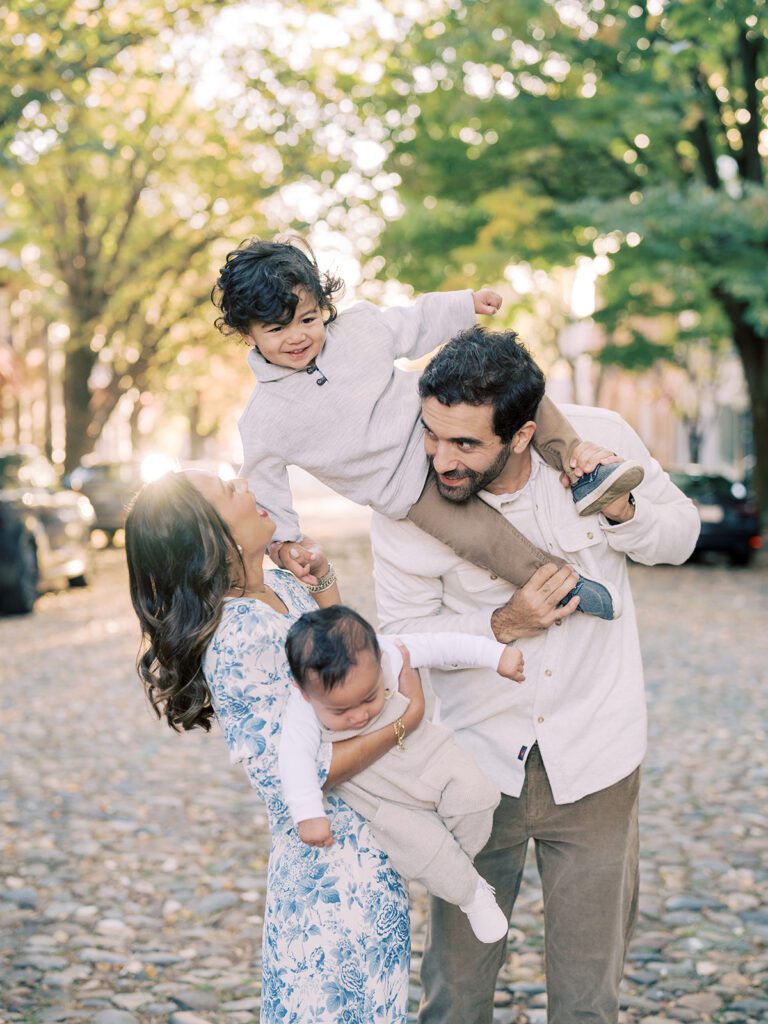 A father has his young son on his shoulders and leans into his wife who is holding their baby during their family photos in Old Town Alexandria.