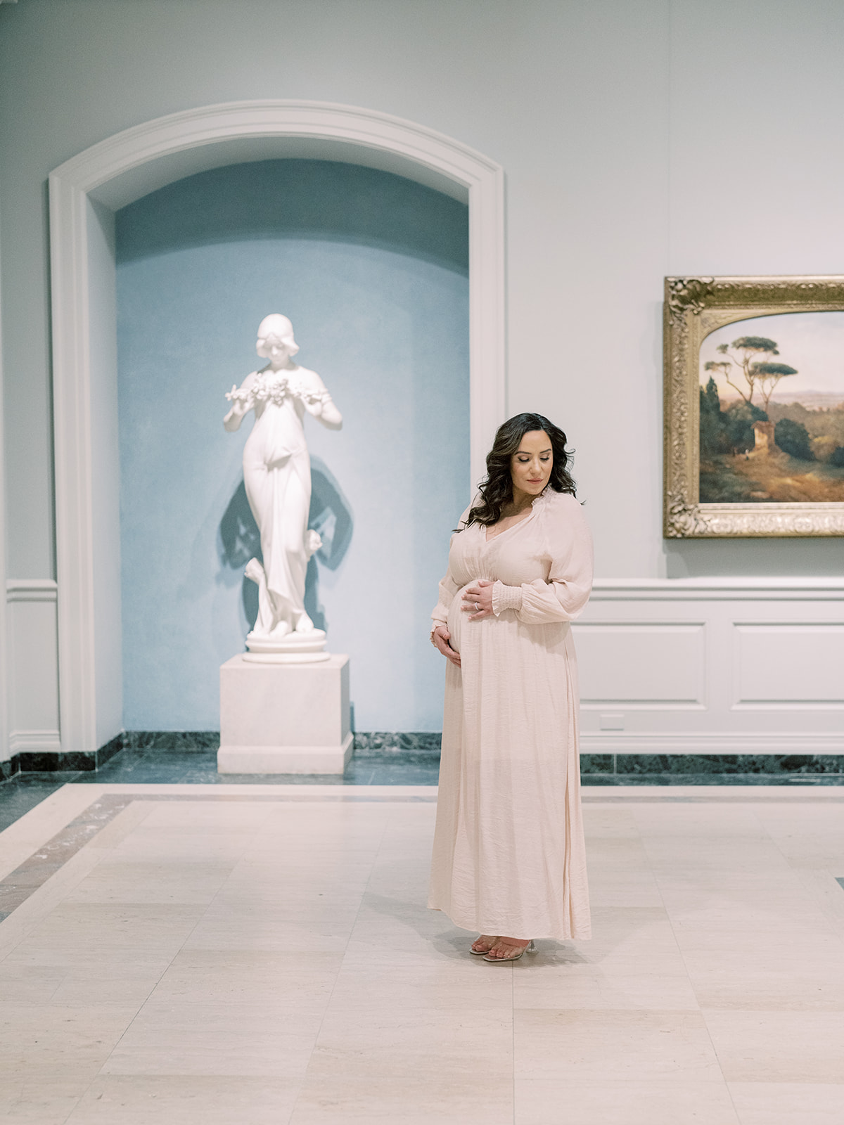 Brown-Haired Woman Stands In The National Gallery Of Art During Her Maternity Session.