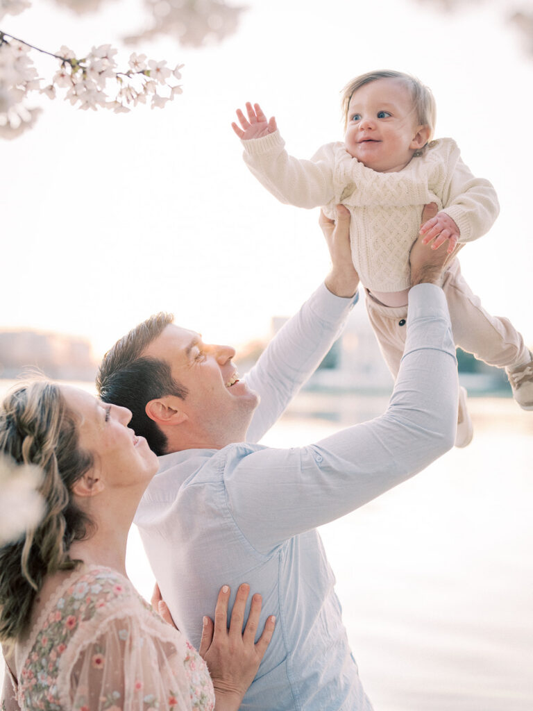 Mother And Father Hold Baby Boy Up To Cherry Blossoms.