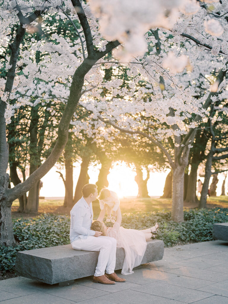 Family Sitting On Bench At Tidal Basin During Their Dc Cherry Blossoms Family Session.