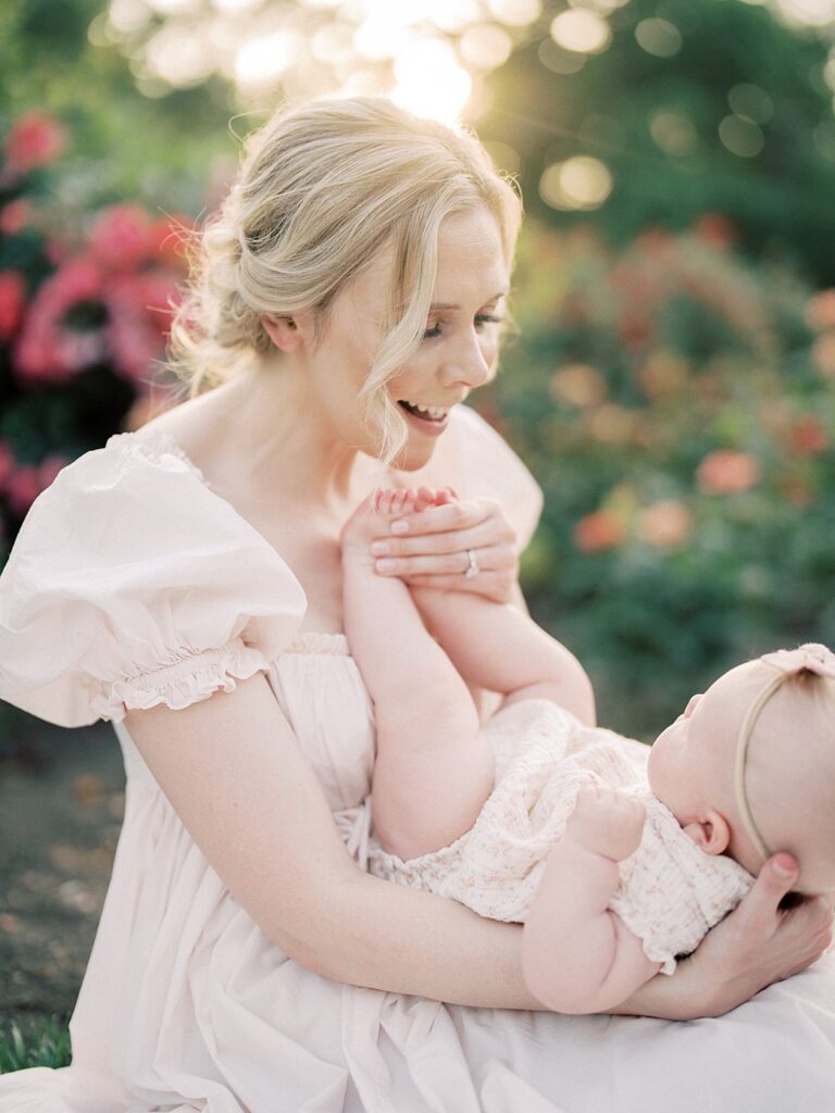 A Blonde Mother Holds Her Baby On Her Lap And Smiles At Her During Their Arlington Family Photos.