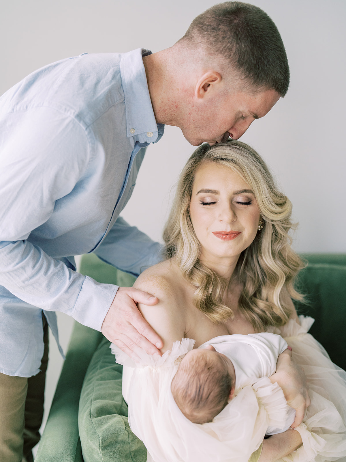 Father Leans Over To Kiss His Blonde Wife Who Holds Their Newborn Baby, Photographed By Bethesda Newborn Photographer Marie Elizabeth Photography