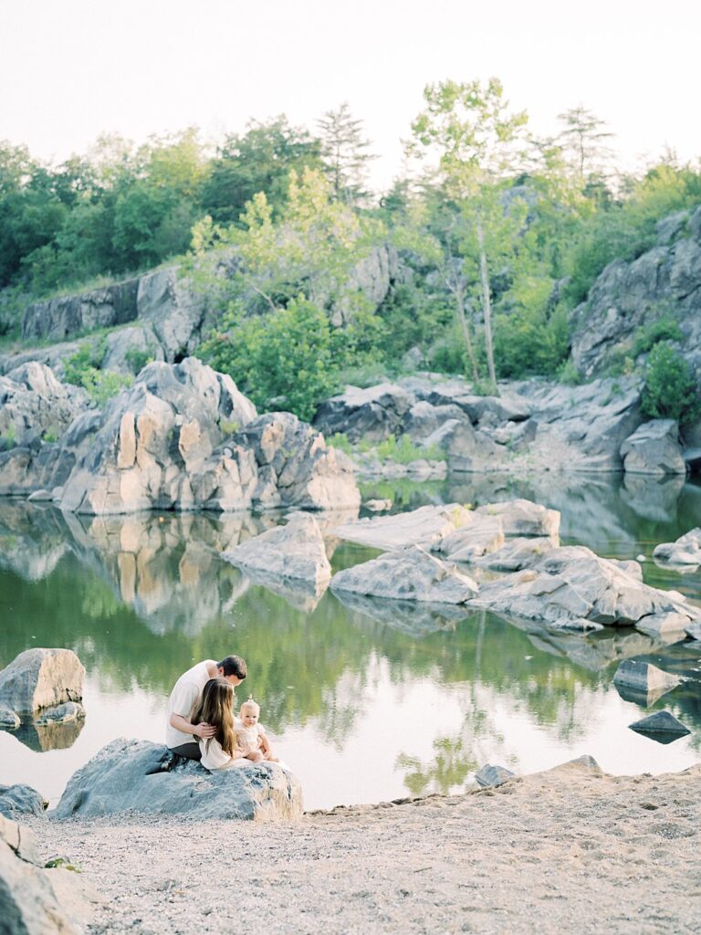 A Pulled Back Image Of A Family Sitting On A Rock At A Great Falls Beach In Maryland.