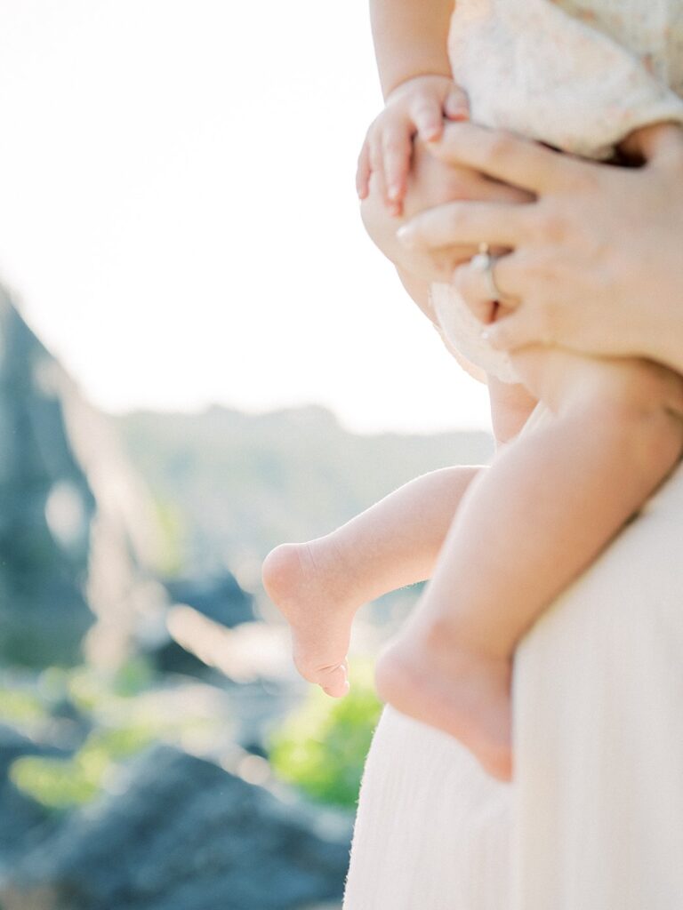 A Close-Up View Of Baby Legs Dangling Off Of A Mom's Hip.