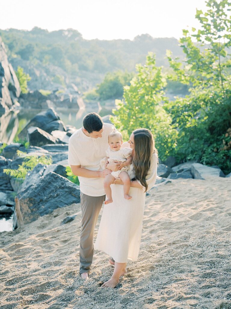 A Father And Mother Hold Their One Year Old Daughter While She Smiles At Great Falls Beach In Maryland. 