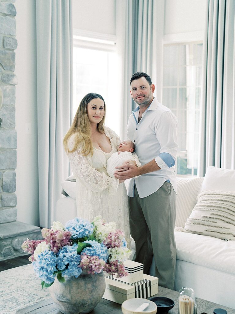 New Mother And Father Stand In Their Living Room Holding Their Newborn Baby Boy During Their Olney Newborn Photos.