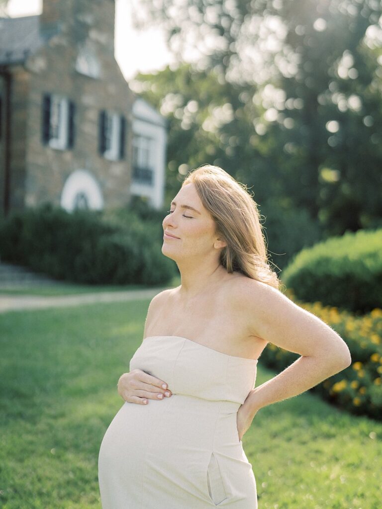 Pregnant Mom Stands In Front Of Glenview Mansion With One Hand On Her Belly And The Other Behind Her Back, Photographed By One Of The Best Rockville Md Family Photographers, Marie Elizabeth Photography.