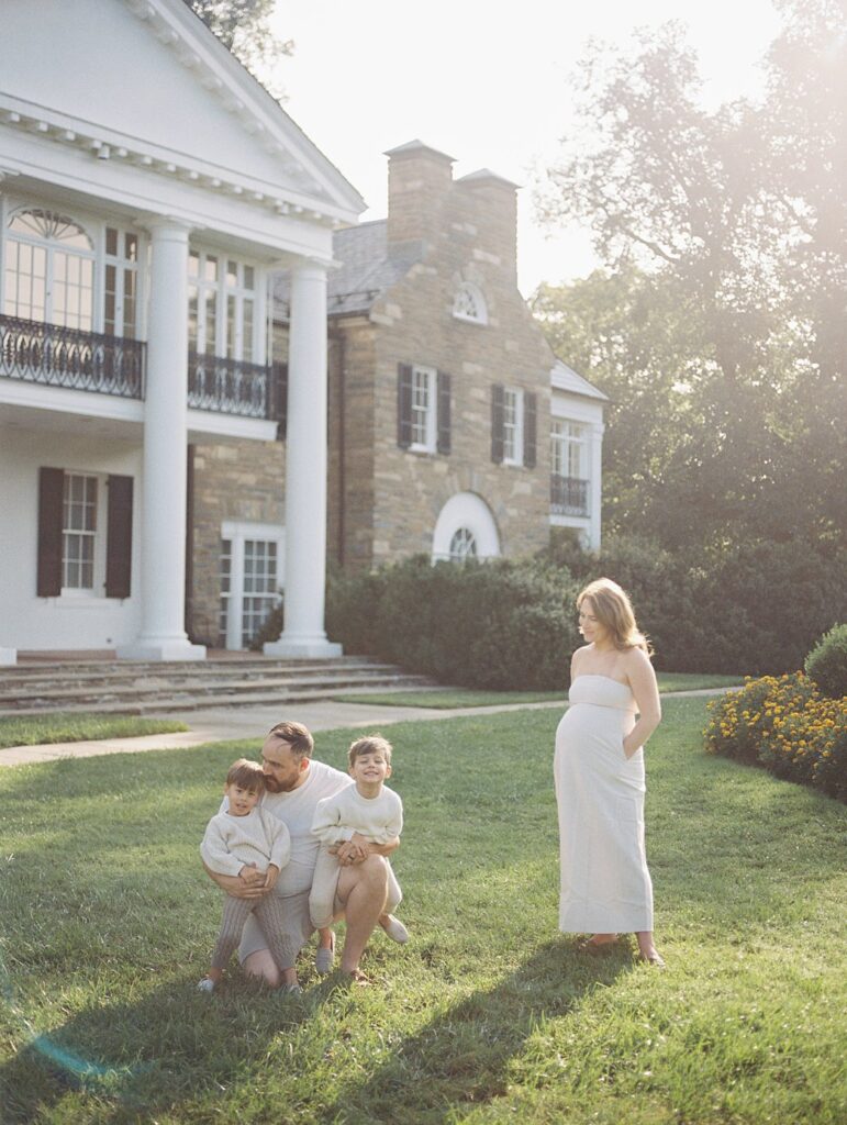 Mother Stand With Her Hands In Her Pockets As Her Husband Crouches With Their Sons During Their Rockville Family Photos.