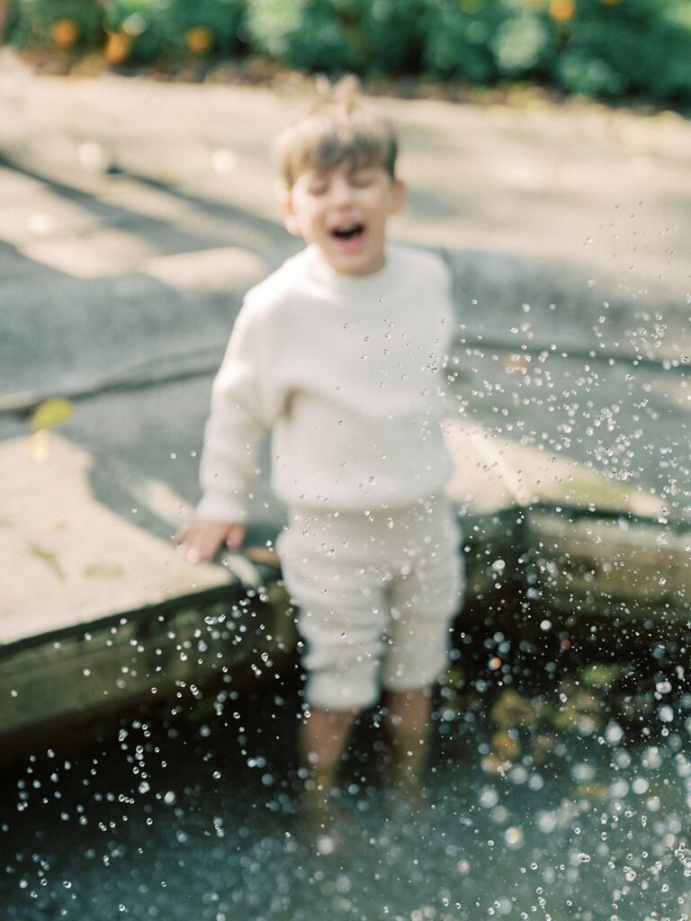 Little Boy Splashes In A Fountain.