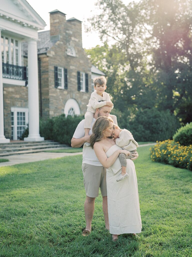 Mother Holds Her Young Son As She Stands With Her Husband Who Has Their Other Son On His Shoulders In Front Of Glenview Manor In Rockville.