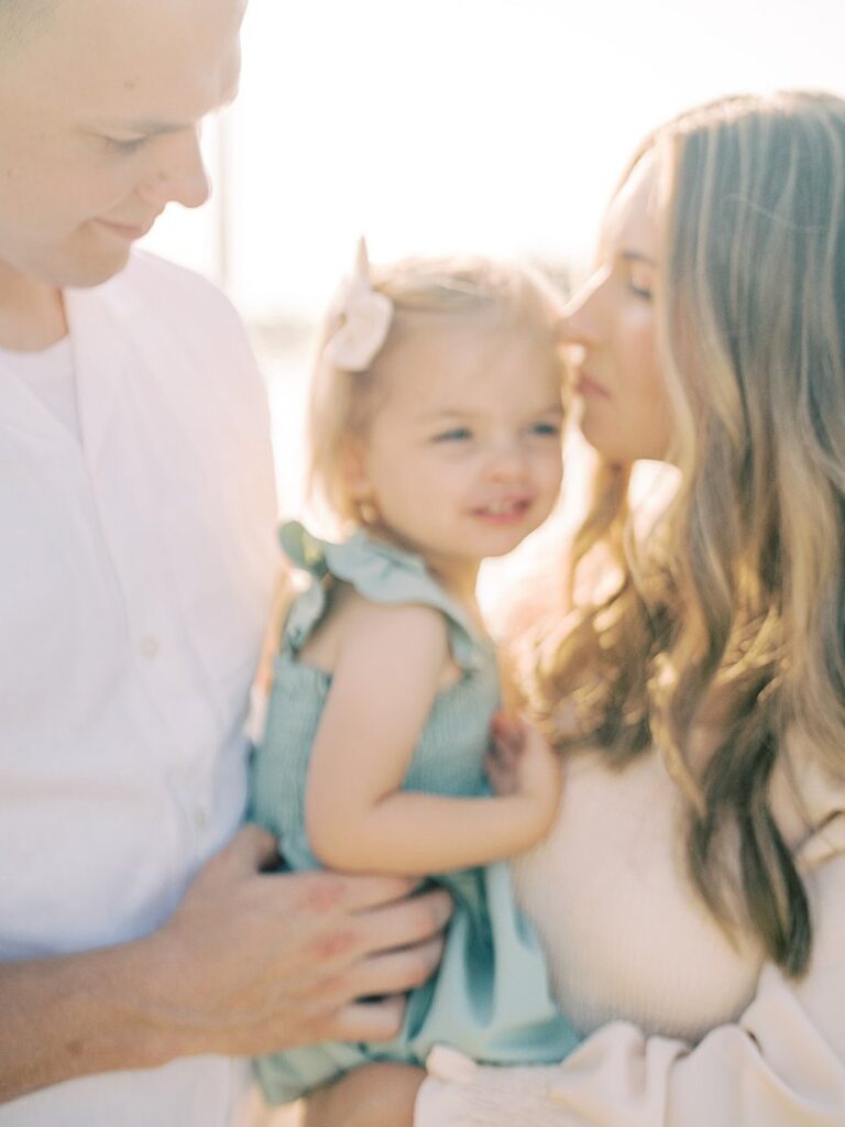 A Blurry Image Of A Mother Cuddling Her Daughter And Husband.