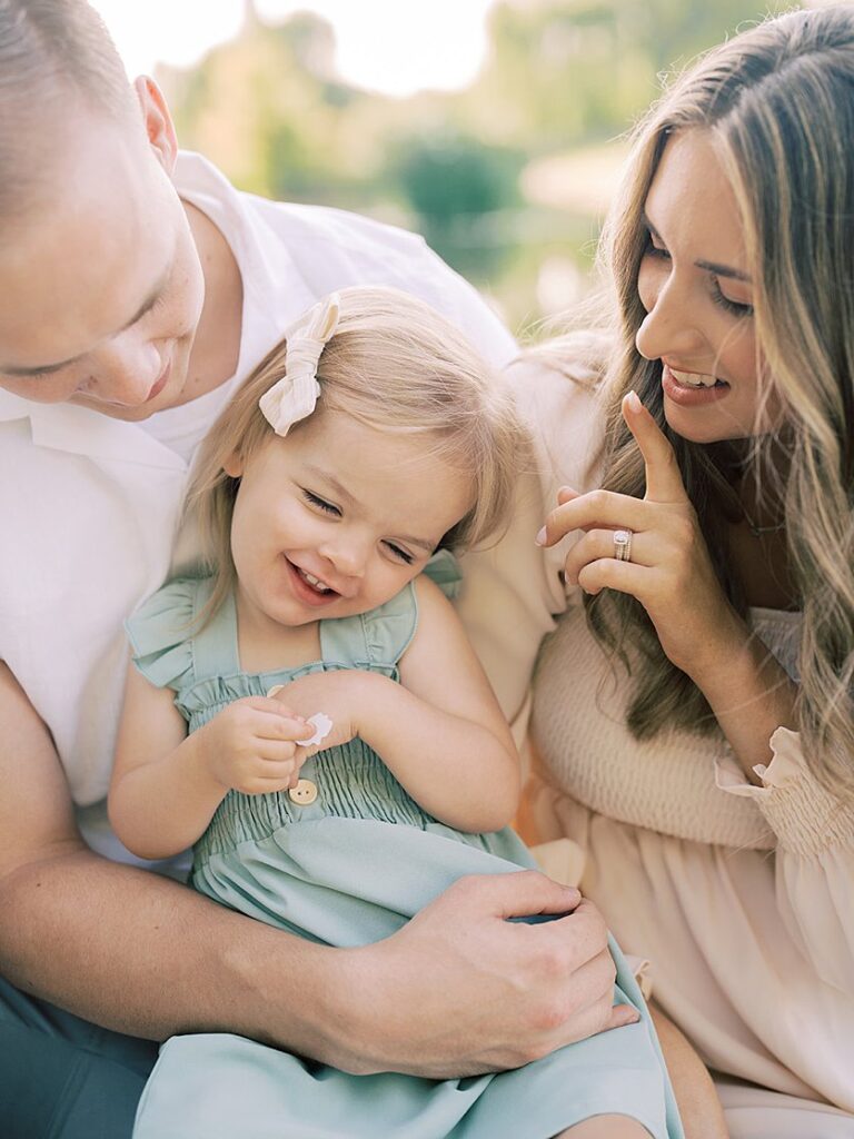 A Mother And Father Sit And Tickle Their Toddler Daughter.