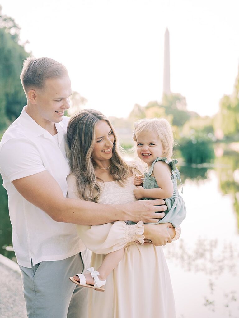 A Father And Mother Smile At Their Little Girl During Their Constitution Gardens Family Photos.