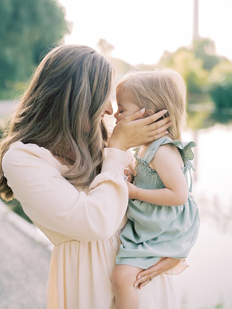 A Mother With Long Brown Hair Holds Her Little Girl's Cheek And Leans Into Her.