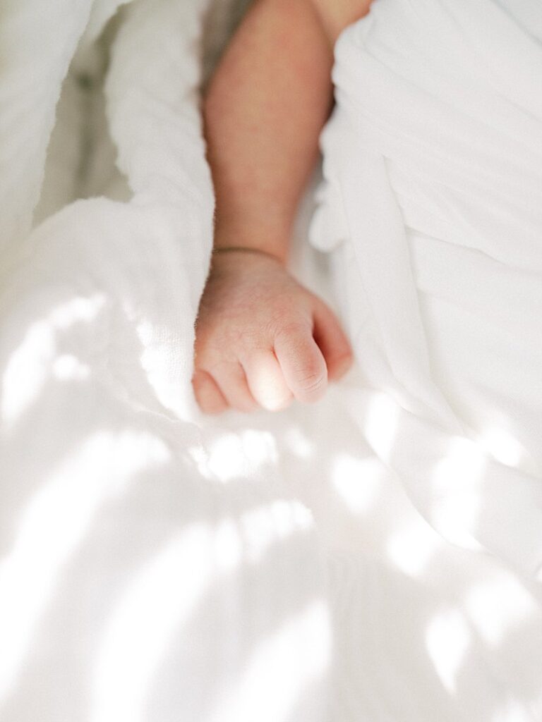 A Close-Up View Of A Baby's Arm And Fingers Against A White Blanket, Photographed During A Falls Church Newborn Photography Session.