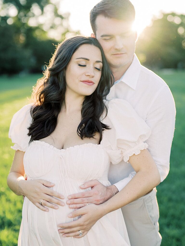 Pregnant Mother Leans Into Her Husband As They Close Their Eyes And Place Their Hands On Her Belly.