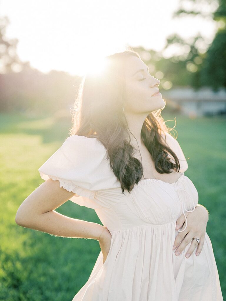 Expecting Mom Places On Hand On Her Stomach And One Hand On Her Back And Gazes Towards The Sky With Eyes Closed.