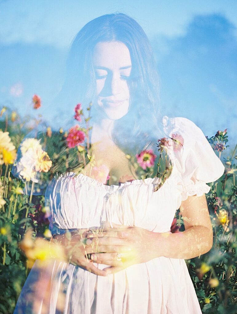 A Maternity Session Double Exposure Of A Pregnant Mother With Her Hands On Her Belly Overlayed With Yellow And Red Flowers.