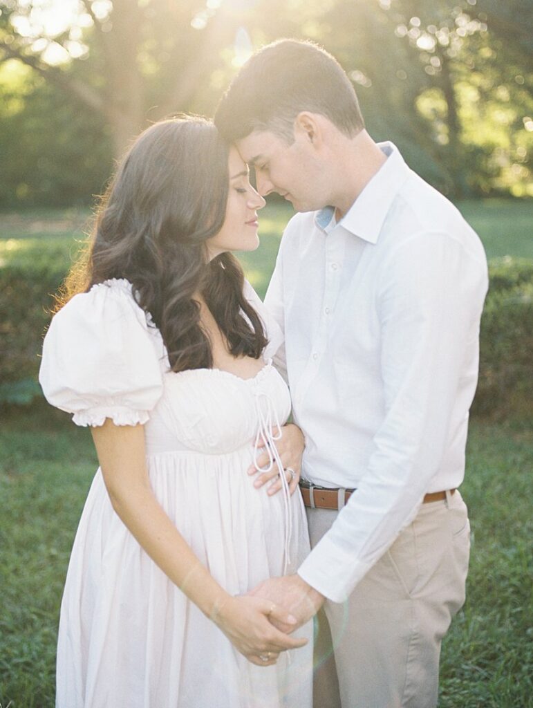 Expecting Parents Hold Hands And Face One Another Head-To-Head During Their Maternity Photos At Sunset.