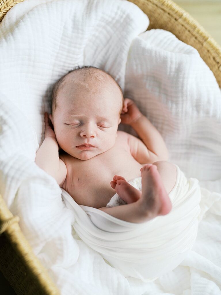 A Newborn Baby Sleeps Peacefully In A Bassinet Swaddled In White.