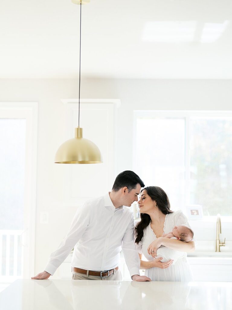 New Parents Lean In Close During While Standing In Their Kitchen Holding Their Baby During Their Severna Park Newborn Photos.