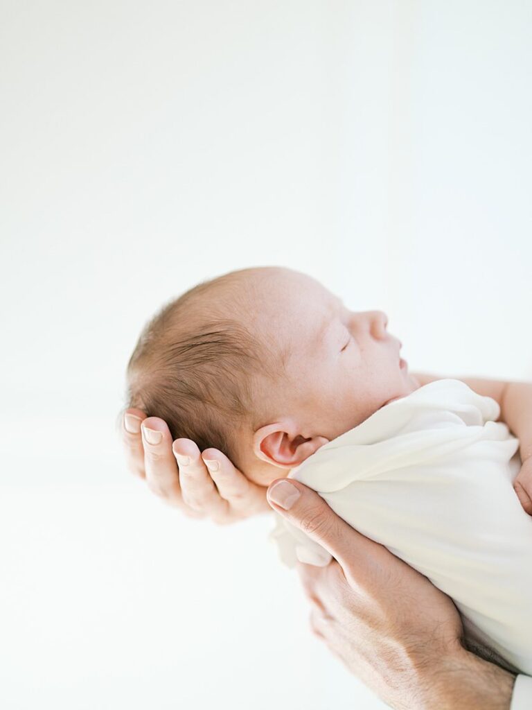 A View Of A Newborn's Head While A Parent Holds Him Out In Front.