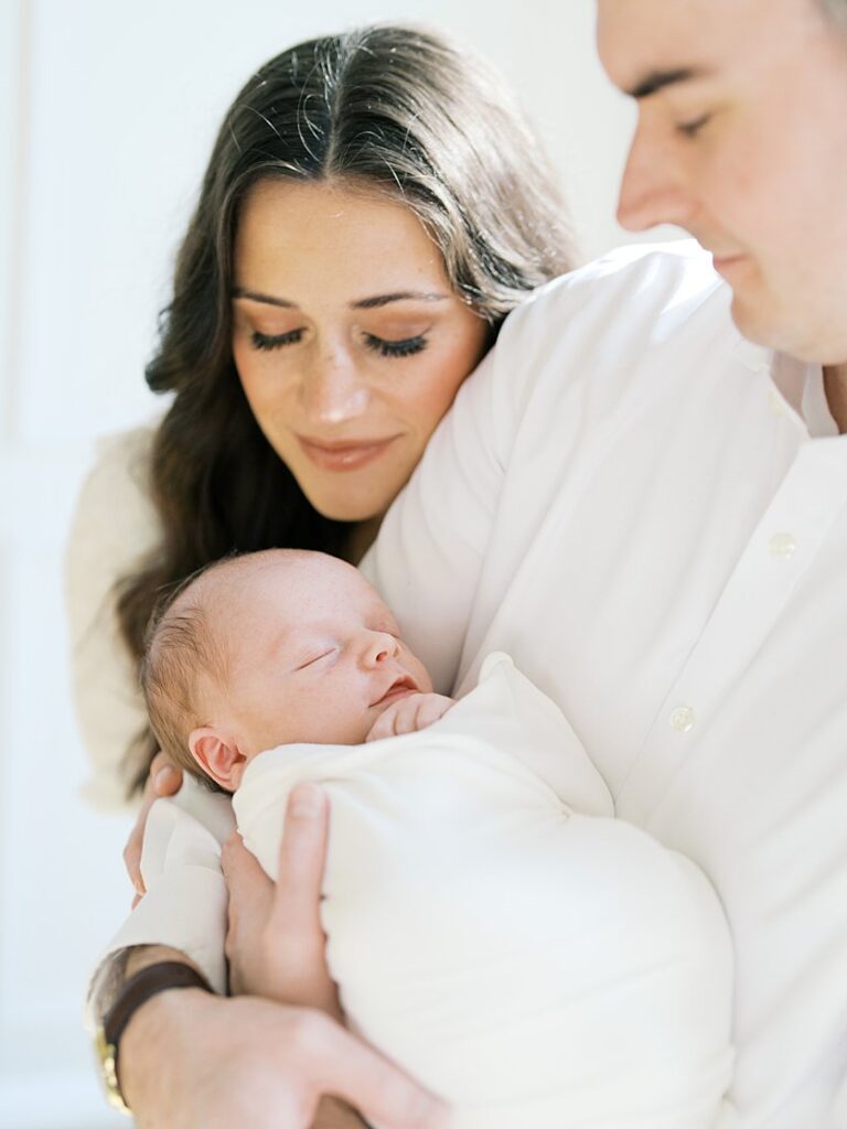 A Mother Leans In To Her Newborn Baby Held By Her Husband.