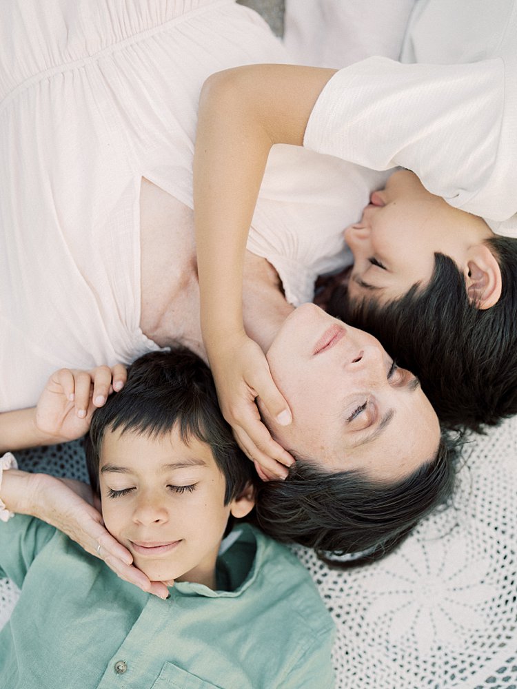 Mother Lays On The Ground With Her Two Sons As They Cuddle Close And Close Their Eyes During Their Great Falls Family Photos.