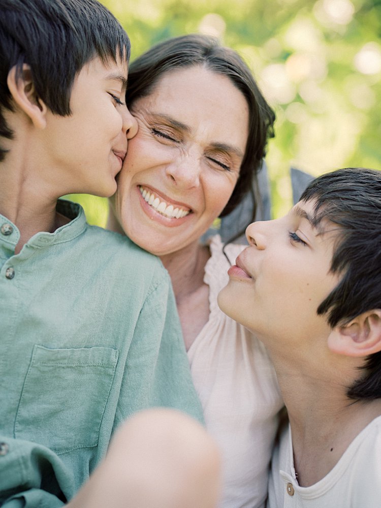 A Mother Smiles Widely As Her Two Boys Nuzzle Close And Give Her A Kiss During Their Great Falls Family Photos.